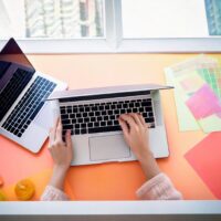 明るいデスクで作業中のWebデザイナー。ノートパソコンやカラーチャートでアイデアを形にしています。